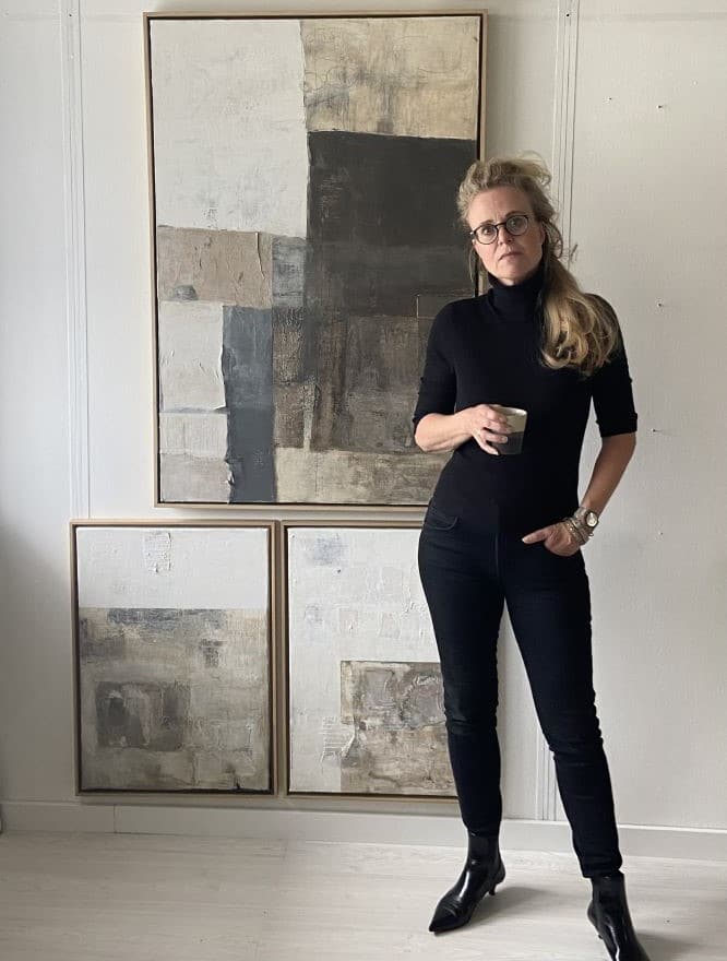 self portrait of artist, Jolanda Wassenaar, in her studio with all the paintings on the wall in the natural colour palette of clay, white and black