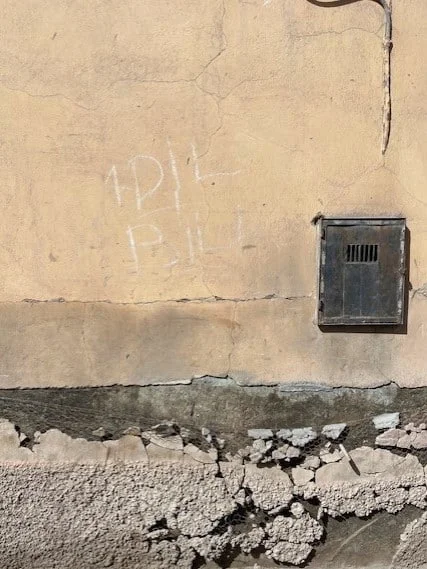 old wall in Marrakech with stucco in warm brown colour, peeled off paint and a tiny wooden door